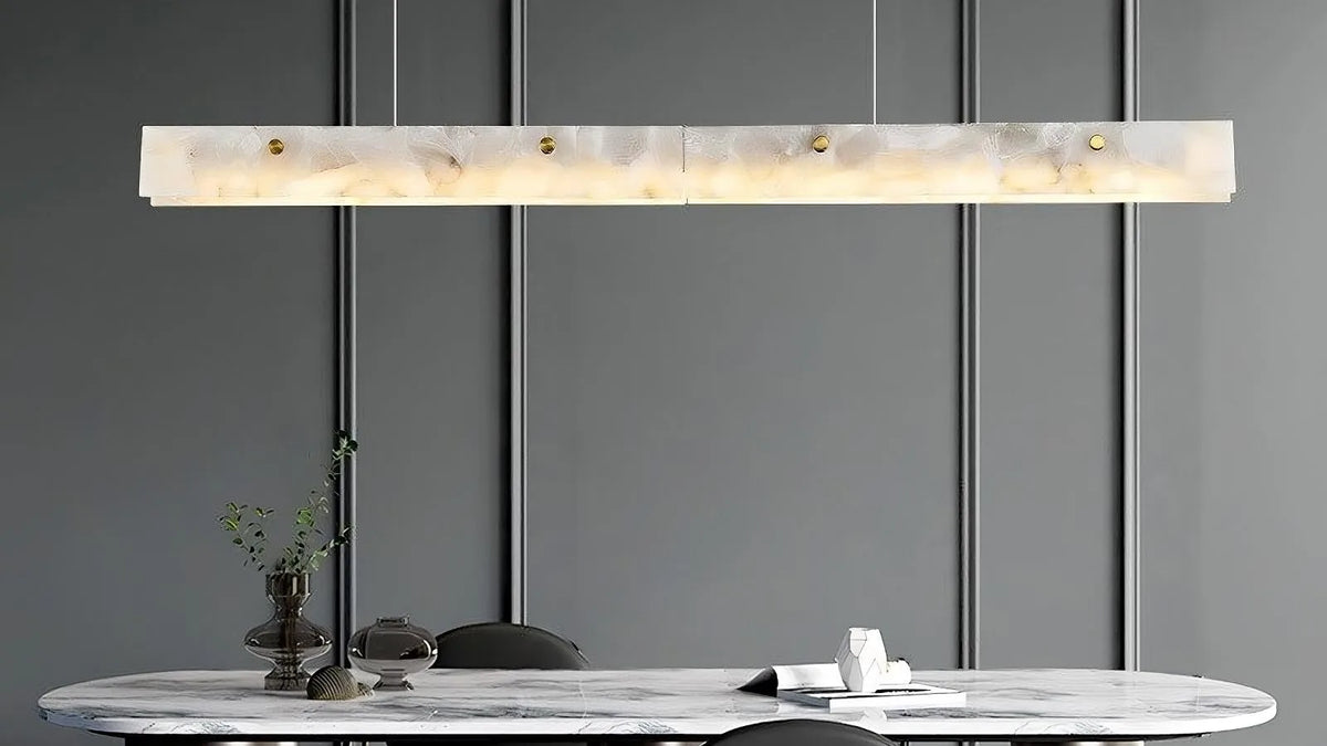Natural marble linear chandelier over a dining table with warm light and slim suspension cables