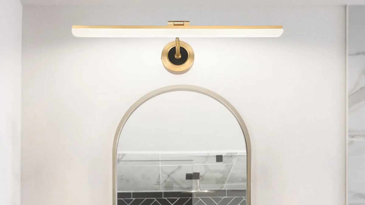 Brass linear bathroom vanity light installed above an arched mirror with warm white illumination